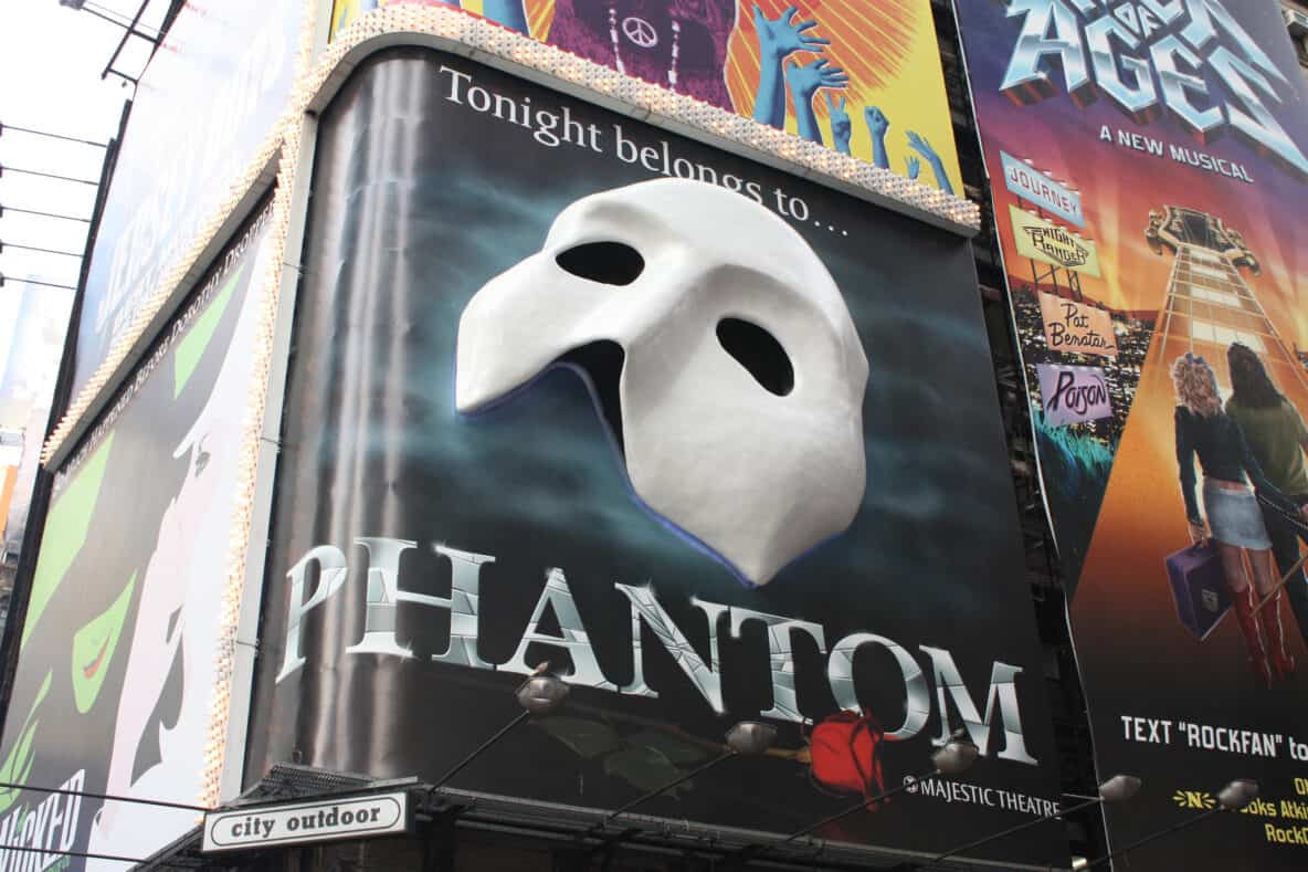 A billboard from the show Phantom of the Opera covers the corner of a building.