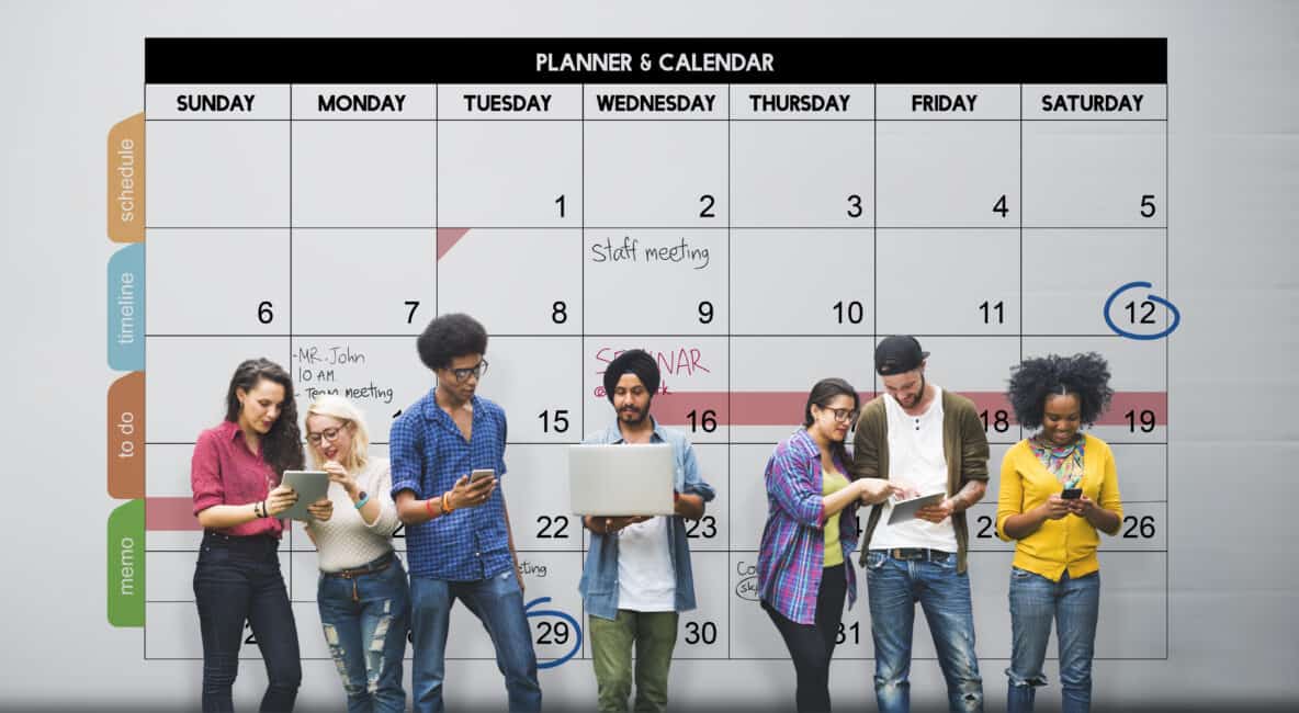 A group of students stand in front of a calendar while working together.