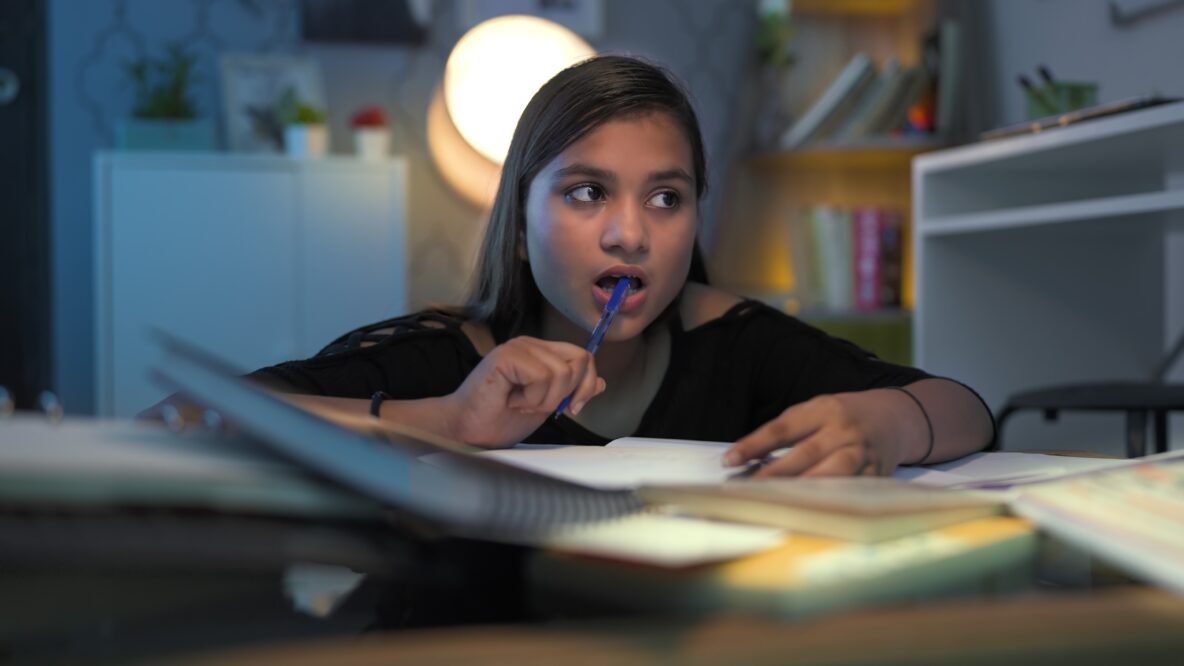 A girl sits at a desk thinking about what to write.