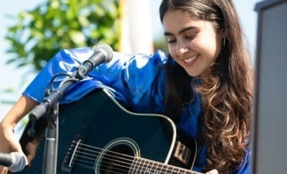 Mila Mincy playing guitar and singing at graduation