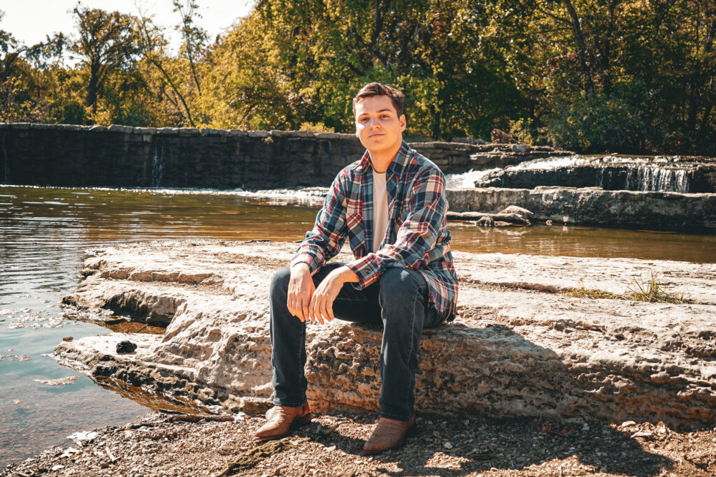 Mario Williams, music student, sits outside in front of a waterfall. 