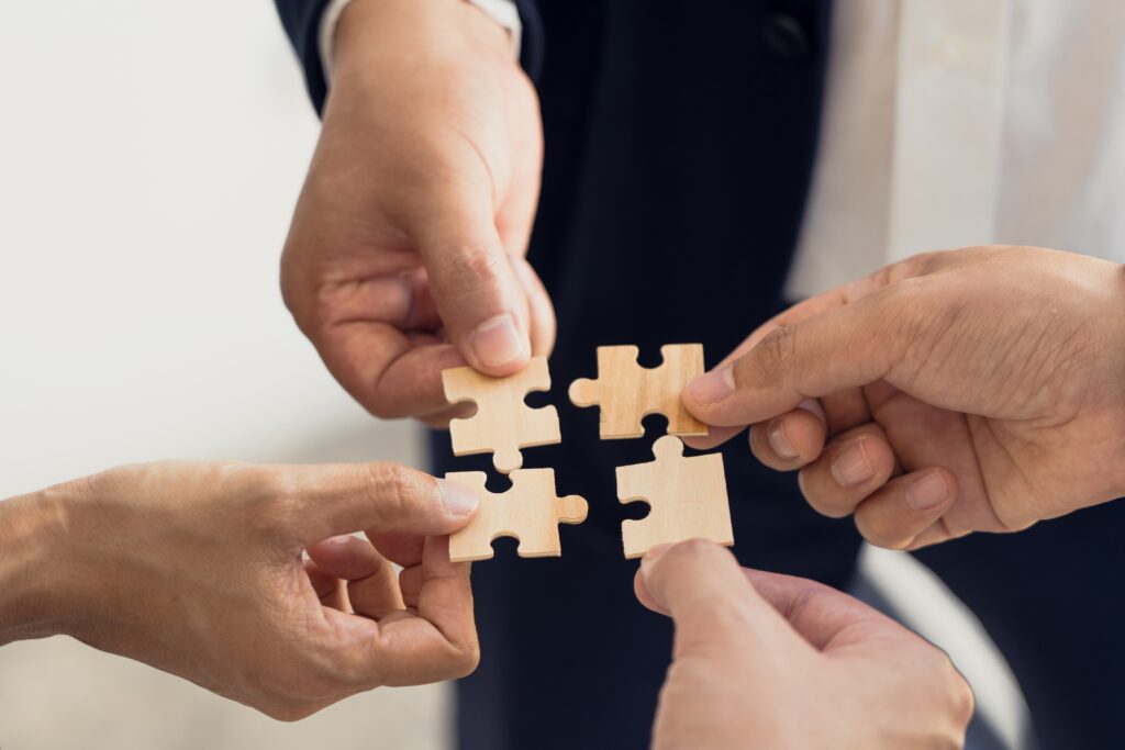 four hands holding puzzle pieces next to each other